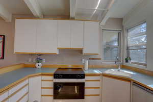 Kitchen featuring black range with electric cooktop, light countertops, stainless steel dishwasher, and two tone cabinetry
