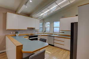 Dual tone kitchen featuring light wood-type flooring, black appliances, light countertops, a breakfast bar, and a peninsula