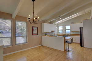 Kitchen with white cabinetry, vaulted ceiling with beams, hanging lights, a peninsula, and a kitchen bar