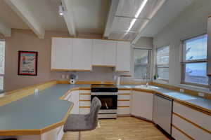 Two tone kitchen with white range with electric stovetop, stainless steel dishwasher, light countertops, light wood finished floors, and dual tone cabinetry