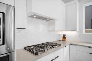 Kitchen with white cabinets, stainless steel appliances, light stone counters, and decorative backsplash