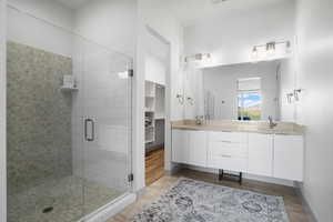 Full bathroom with double vanity, a stall shower, and dark wood-type flooring