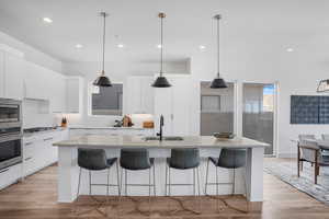 Kitchen with white cabinets, stainless steel appliances, light wood-style floors, pendant lighting, and modern cabinets
