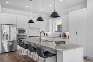 Kitchen with stainless steel appliances, white cabinetry, modern cabinets, light stone countertops, and dark wood finished floors