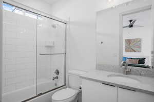 Bathroom with vanity, bath / shower combo with glass door, ensuite bath, and ceiling fan