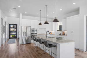 Kitchen with stainless steel appliances, a breakfast bar area, white cabinetry, light wood-type flooring, and an island with sink