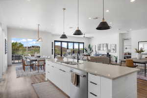 Kitchen with white cabinetry, light wood-style floors, light stone countertops, a kitchen island with sink, and hanging light fixtures