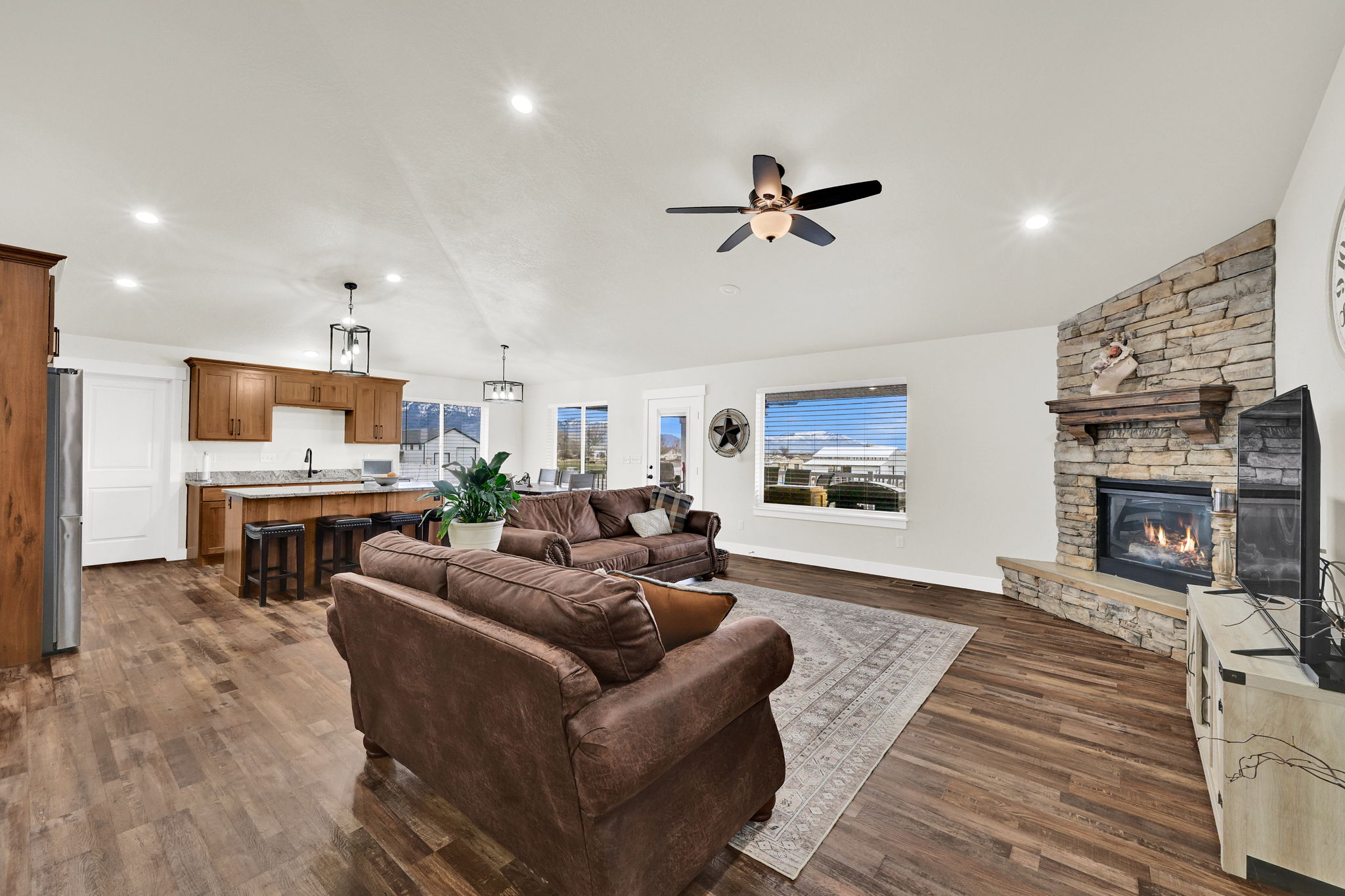 Living area featuring dark wood finished floors, a stone fireplace, ceiling fan, healthy amount of natural light, and recessed lighting