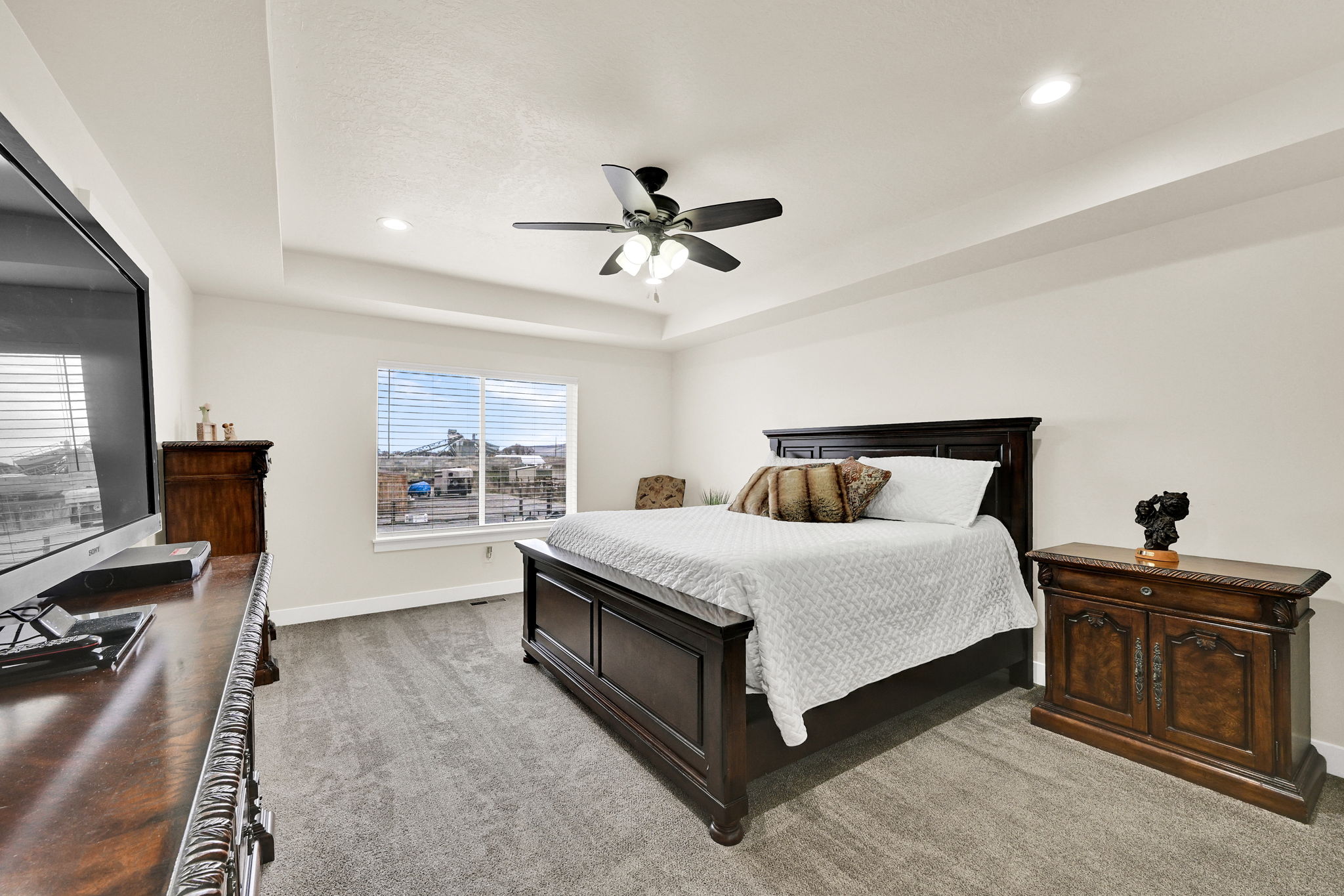 Bedroom featuring light carpet, a ceiling fan, recessed lighting, and a raised ceiling