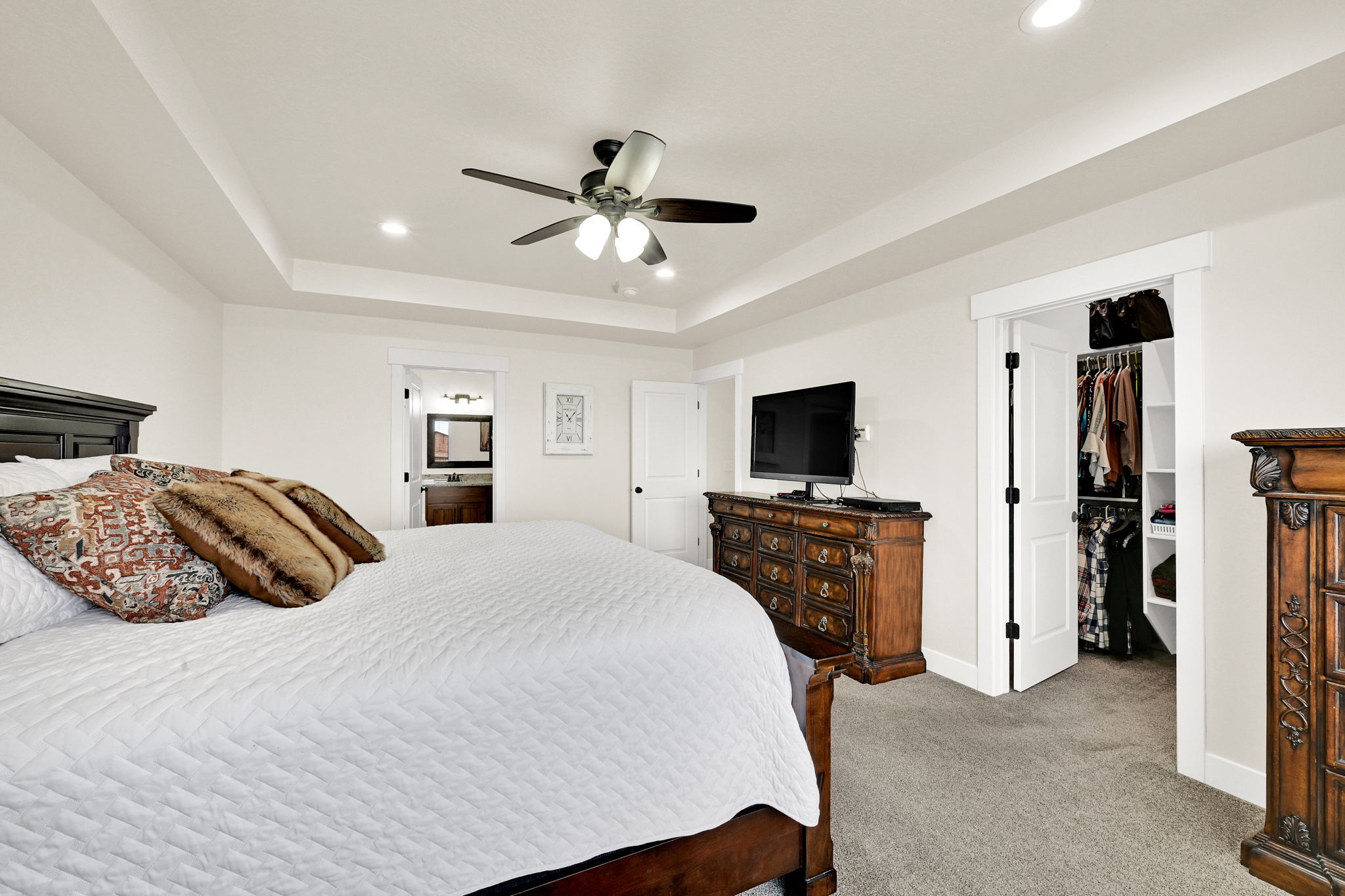Bedroom with recessed lighting, a walk in closet, light colored carpet, a ceiling fan, and a raised ceiling