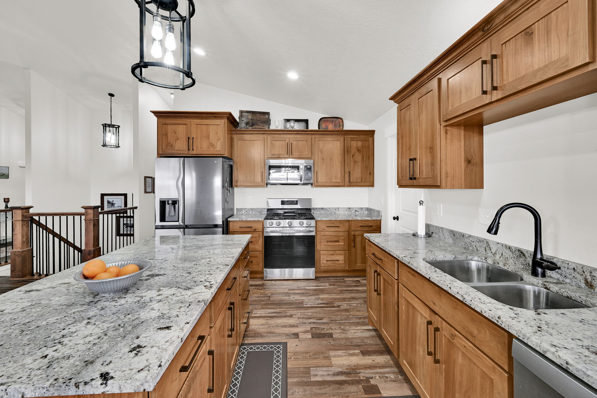 Kitchen featuring light stone countertops, vaulted ceiling, stainless steel appliances, dark wood-style flooring, and decorative light fixtures