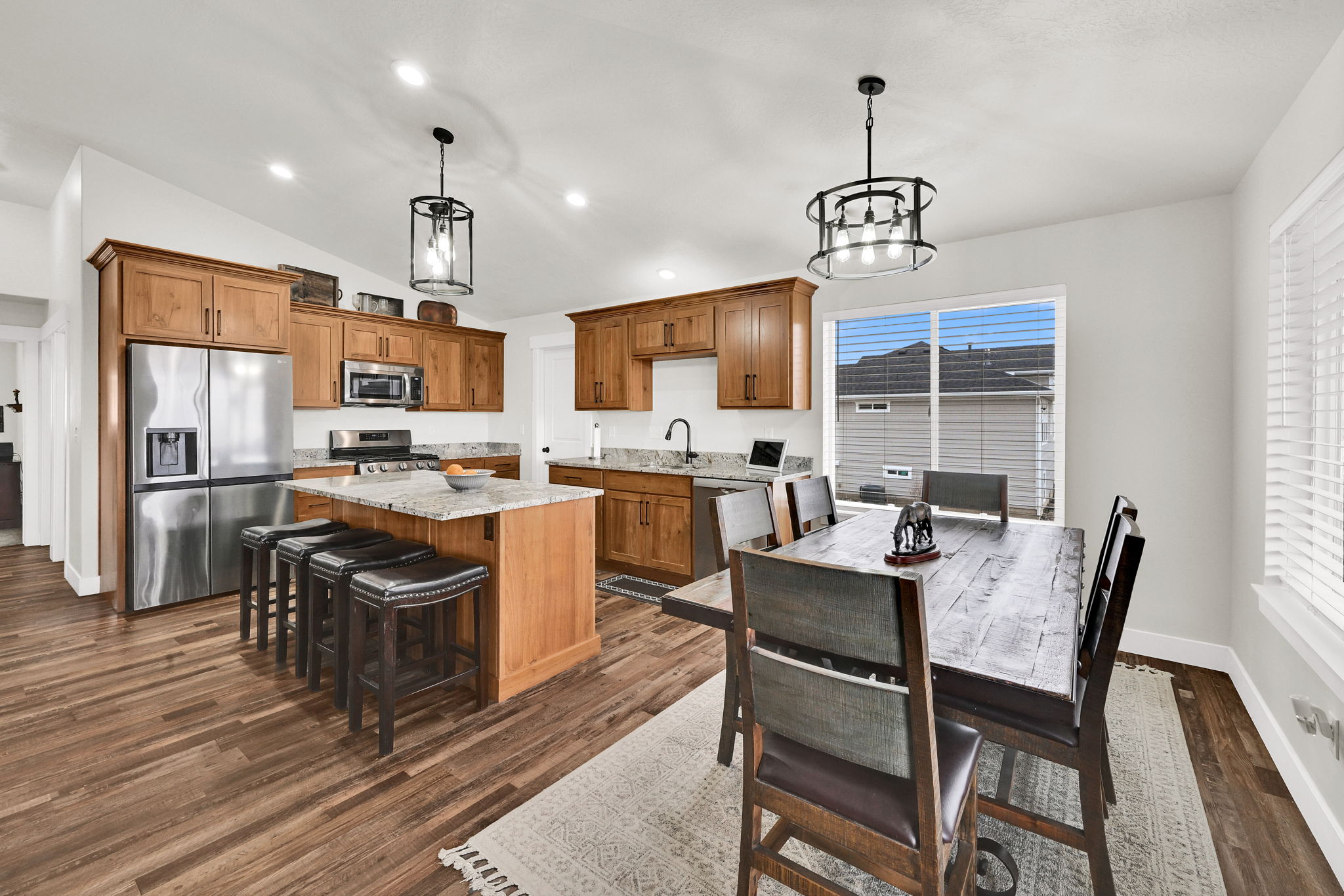 Kitchen featuring wood finish cabinets, stainless steel appliances, light stone countertops, a kitchen island, and vaulted ceiling