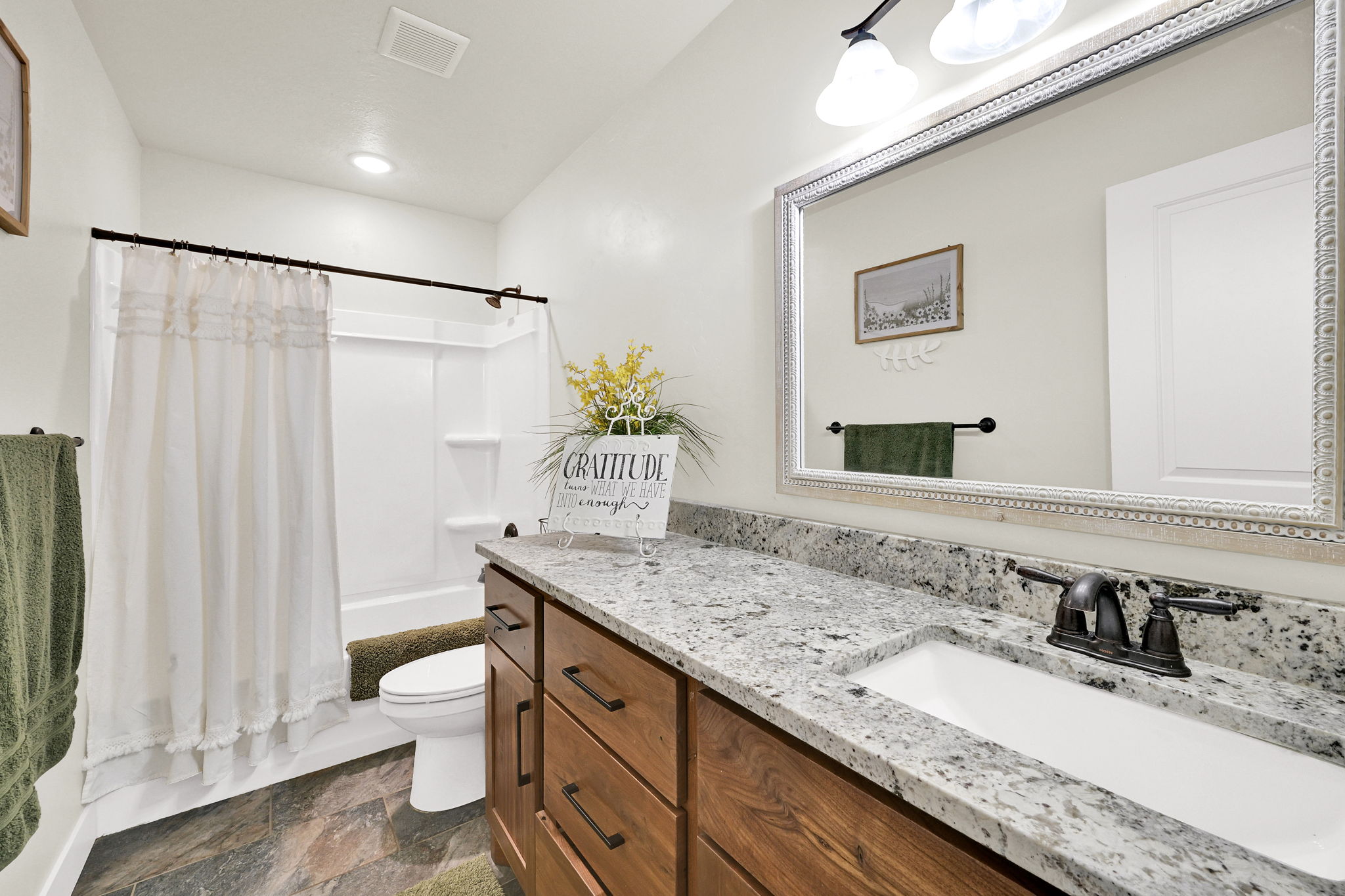 Bathroom featuring vanity, shower / bath combo with shower curtain, and stone finish flooring