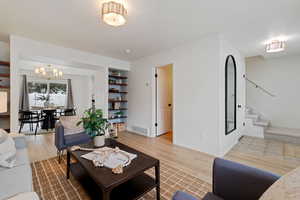Living room featuring light wood-style flooring, a chandelier, and built in features
