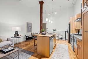 Kitchen with a high ceiling, wood counters, a kitchen breakfast bar, an island with sink, and light wood-type flooring