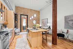 Kitchen with brick wall, a kitchen island with sink, light wood finish cabinetry, light wood finished floors, and pendant lighting