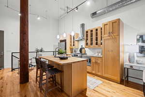 Kitchen with a high ceiling, an island with sink, wood counters, exhaust hood, and light wood-style floors