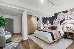 Bedroom featuring rail lighting, finished concrete flooring, and an accent wall