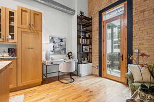 Home office with light wood-style floors, brick wall, and a high ceiling