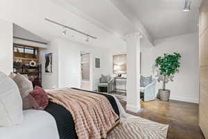 Bedroom featuring concrete floors, track lighting, ensuite bath, and electric panel
