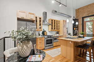 Kitchen with brick wall, a breakfast bar area, an island with sink, stainless steel appliances, and light wood finish cabinets