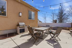 Fenced backyard with outdoor dining space, a patio area, and a grill. Window well covers