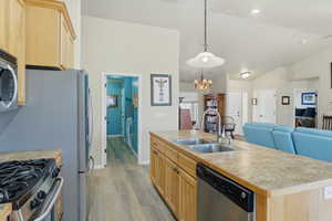 Kitchen featuring light wood finish cabinets, light countertops, stainless steel appliances, open floor plan, and vaulted ceiling