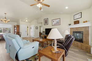 Living area featuring a fireplace, light wood-type flooring, ceiling fan, a chandelier, and a high ceiling