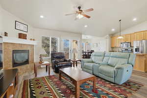 Living room featuring vaulted ceiling, a fireplace, recessed lighting, ceiling fan, and light wood-style floors