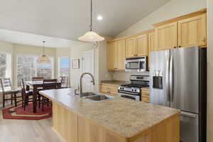 Kitchen with light wood finish cabinets, stainless steel appliances, hanging light fixtures, a kitchen island with sink, and light countertops
