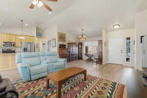 Living area with a ceiling fan, hanging lights, light wood finished floors, and vaulted ceiling