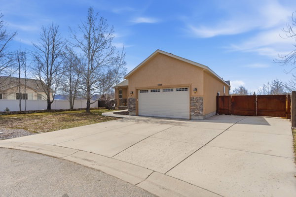 View of side of property featuring an attached garage, stone siding, a gate, stucco siding, and concrete driveway