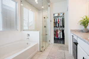 Full bath featuring vanity, a stall shower, a garden tub, a spacious closet, and light tile patterned floors