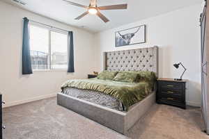 Bedroom with ceiling fan, a barn door, and light carpet