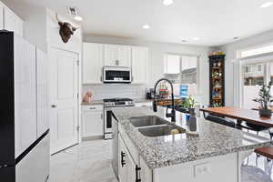 Kitchen with stainless steel appliances, light stone counters, white cabinetry, tasteful backsplash, and light marble finish flooring