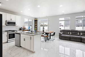 Kitchen featuring light stone counters, a center island with sink, stainless steel appliances, open floor plan, and backsplash