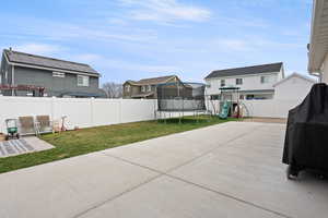 Fenced backyard with a playground, a patio area, a trampoline, and a residential view