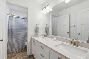 Bathroom with double vanity, a shower with shower curtain, and dark wood-style flooring