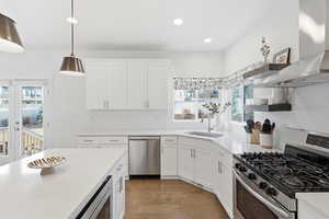Kitchen featuring stainless steel appliances, white cabinetry, light wood-style floors, pendant lighting, and light stone counters