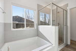 Full bath featuring a stall shower, a bath, and wood finished floors