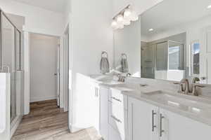 Full bath with double vanity, a stall shower, and light wood-style floors