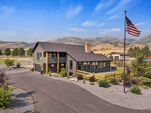 View of front of property with a mountain view, a shingled roof, an attached garage, a chimney, and asphalt driveway