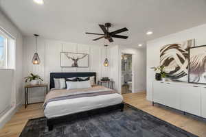 Bedroom with light wood-style floors, a decorative wall, a ceiling fan, connected bathroom, and recessed lighting