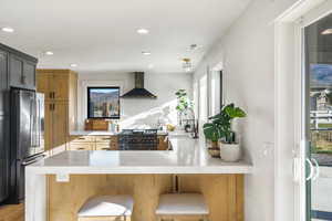 Kitchen with light stone counters, a peninsula, freestanding refrigerator, gas range oven, and a kitchen breakfast bar