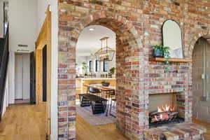 Corridor with light wood-style flooring, arched walkways, hanging lights, and brick wall