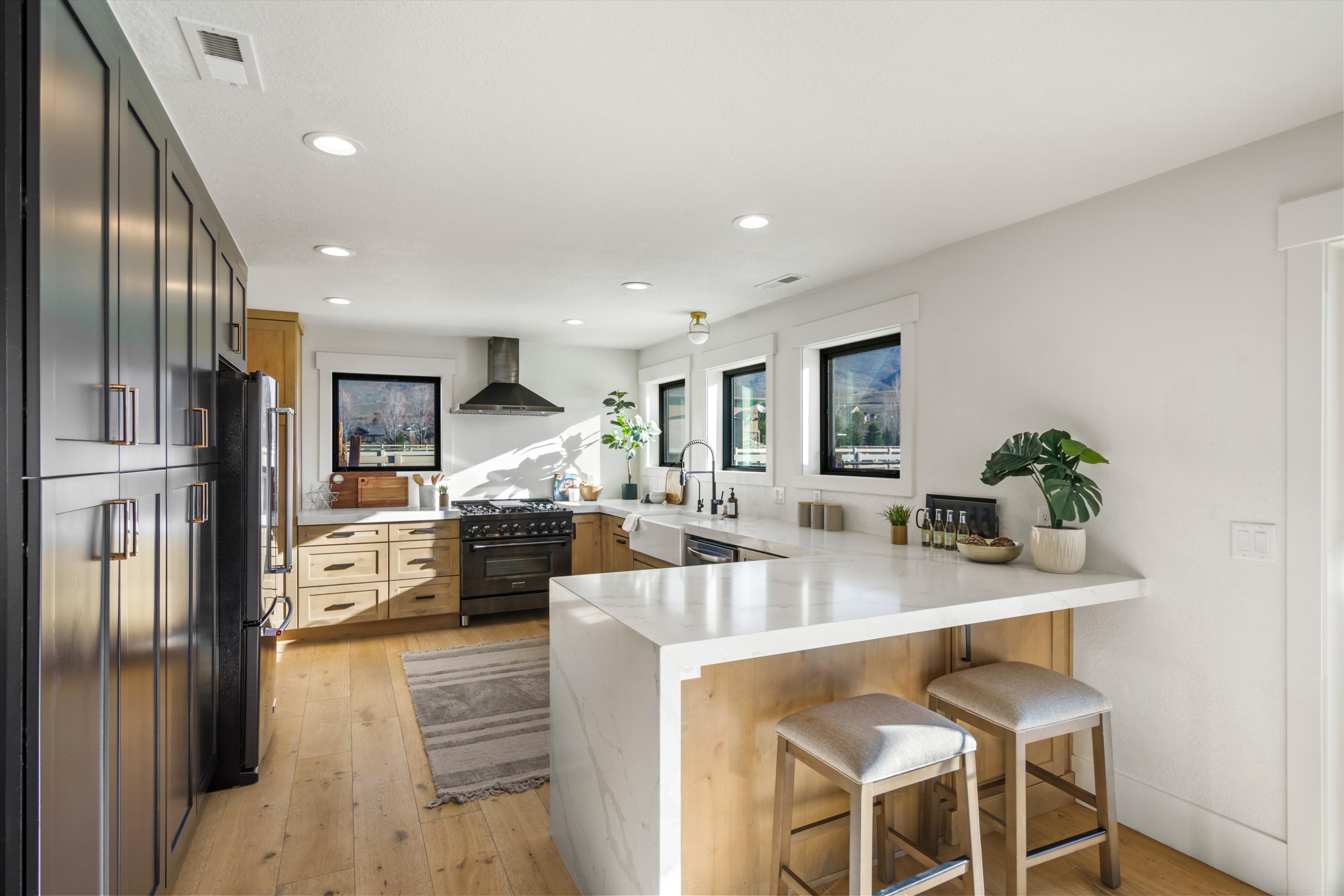 Kitchen with a peninsula, light wood-style floors, black appliances, a kitchen bar, and light stone countertops
