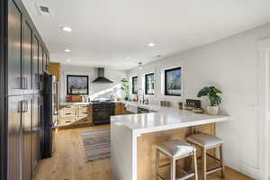 Kitchen with a peninsula, light wood-style floors, black appliances, a kitchen bar, and light stone countertops
