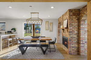 Dining area with a fireplace, light wood-type flooring, brick wall, and suspended lighting