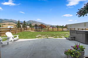 Fenced backyard featuring a trampoline, a patio area, a mountain view, and a hot tub