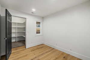 Unfurnished bedroom with light wood-type flooring, a spacious closet, and recessed lighting